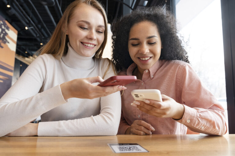 Two women looking at a phone screen with a QR code on the table, representing a conversion.